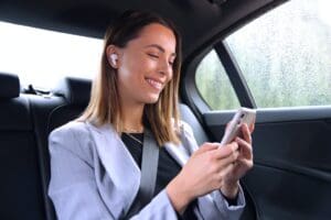 businesswoman with wireless earbuds commuting to work in taxi talking on mobile phone